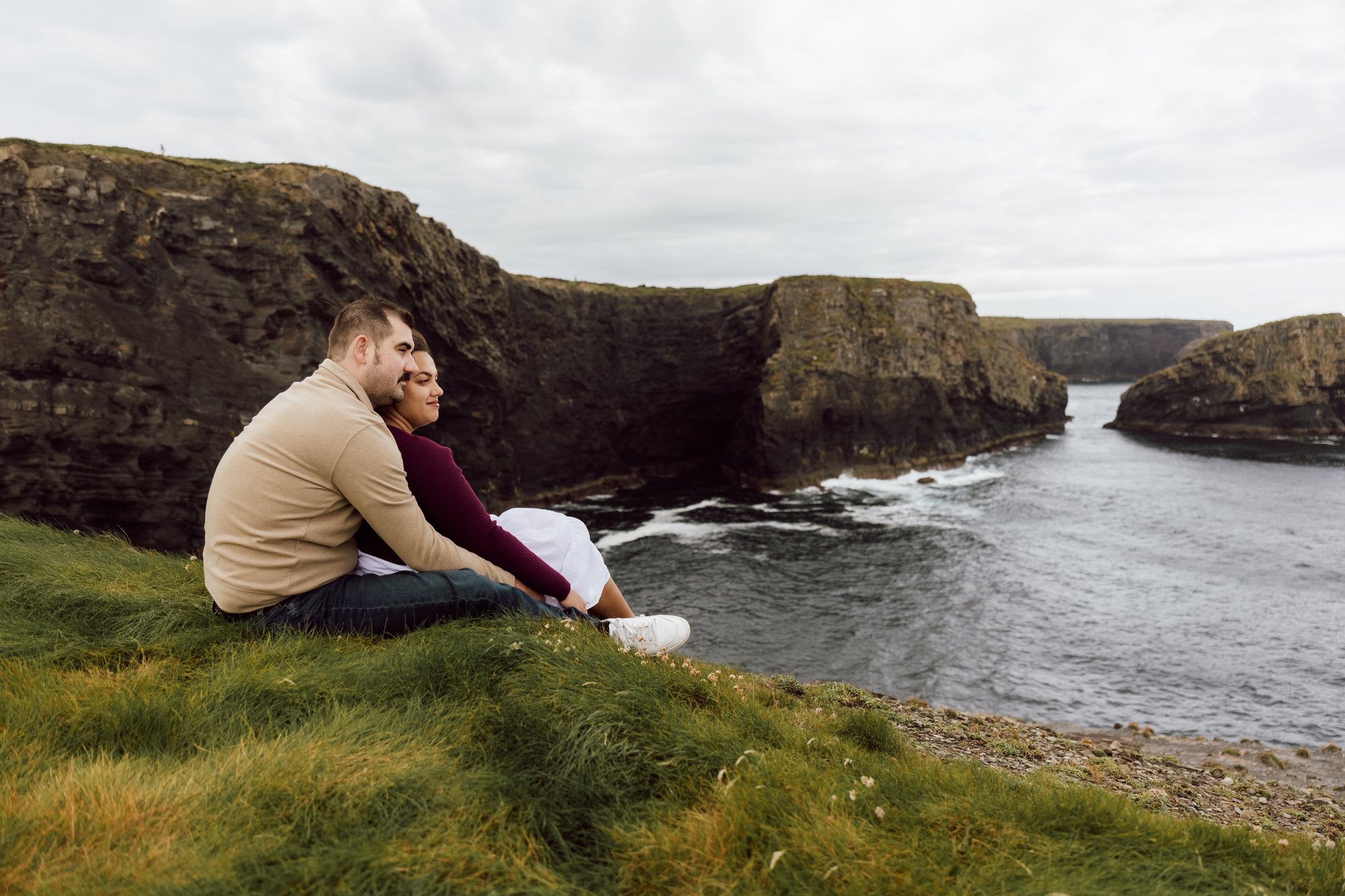 Couple sitting together above a rugged sea inlet